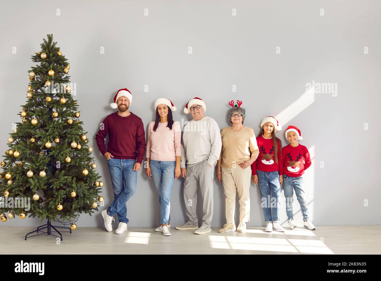 Fröhliche Familie mit mehreren Generationen posiert in Weihnachtsmützen und steht in Reihe neben dem Weihnachtsbaum. Stockfoto