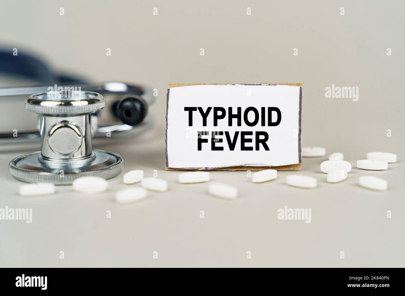 Medizinisches Konzept. Auf grauem Hintergrund ein Stethoskop, Pillen und eine Papptafel mit der Aufschrift - Typhus Fever Stockfoto