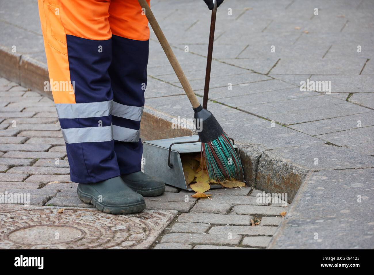 Arbeiter in Uniform mit einem Besen reinigen Sie den Bürgersteig, sammelt abgefallene Blätter in einer Kehrschaufel. Straßenreinigung in der Herbststadt Stockfoto