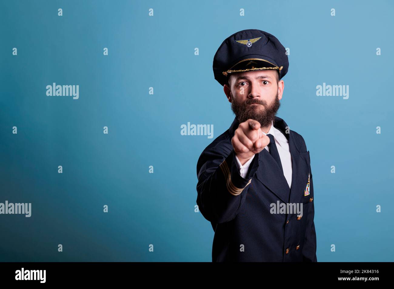 Serious Flugzeug Kapitän zeigt auf Kamera mit Finger, Luftfahrt-Akademie Pilot Ausbildung Rekrutierung. Selbstbewusster Flieger mit professioneller Uniform und Hut im Vorderansicht-Porträt Stockfoto