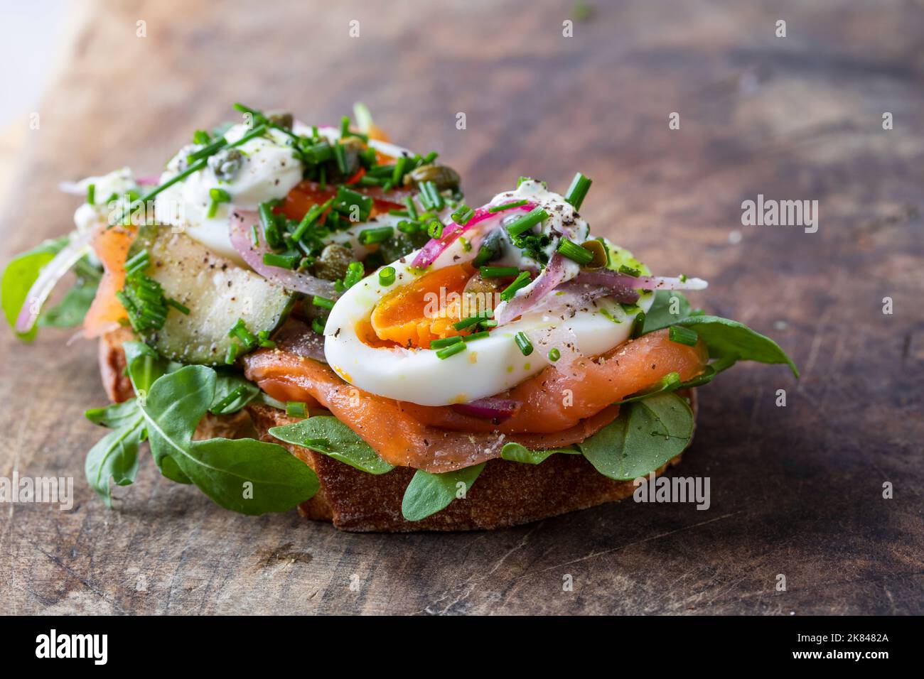 Offenes Sandwich mit geräuchertem Lachs, Ei, eingelegten Zwiebeln, Sauerrahm und Kapern Stockfoto