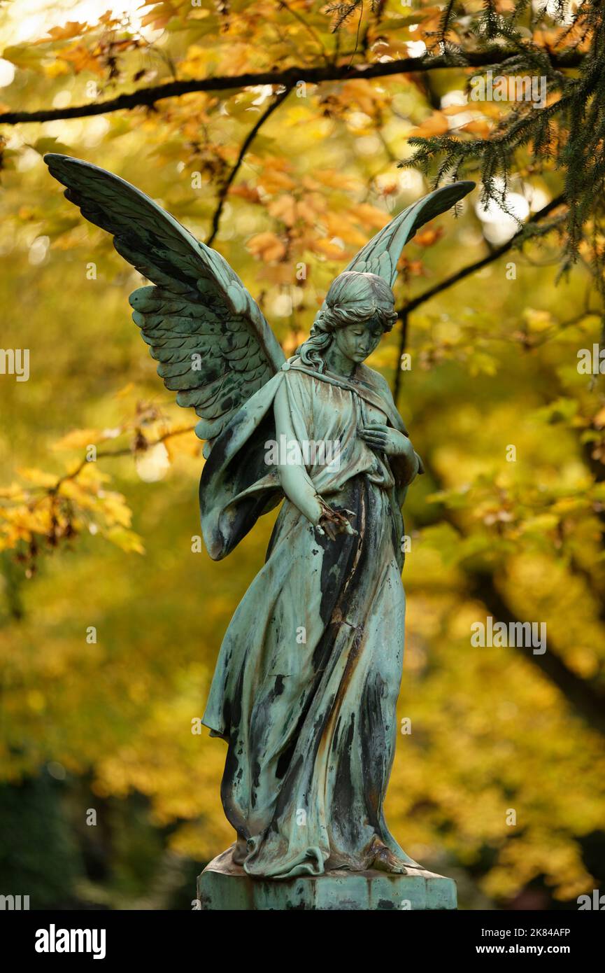 Schöner alter Engel mit Flügeln vor goldenen Herbstblättern auf einem Friedhof Stockfoto