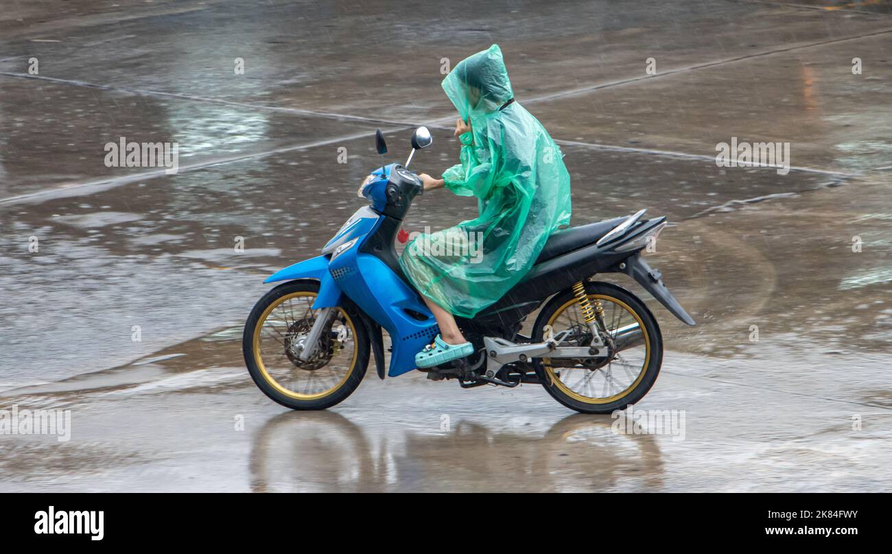 Ein Motorradfahrer im Regenmantel fährt im Regen auf einer Stadtstraße in Thailand Stockfoto