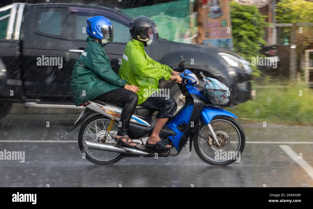 Paar in Regenmänteln fahren im Regen, Thailand Stockfoto