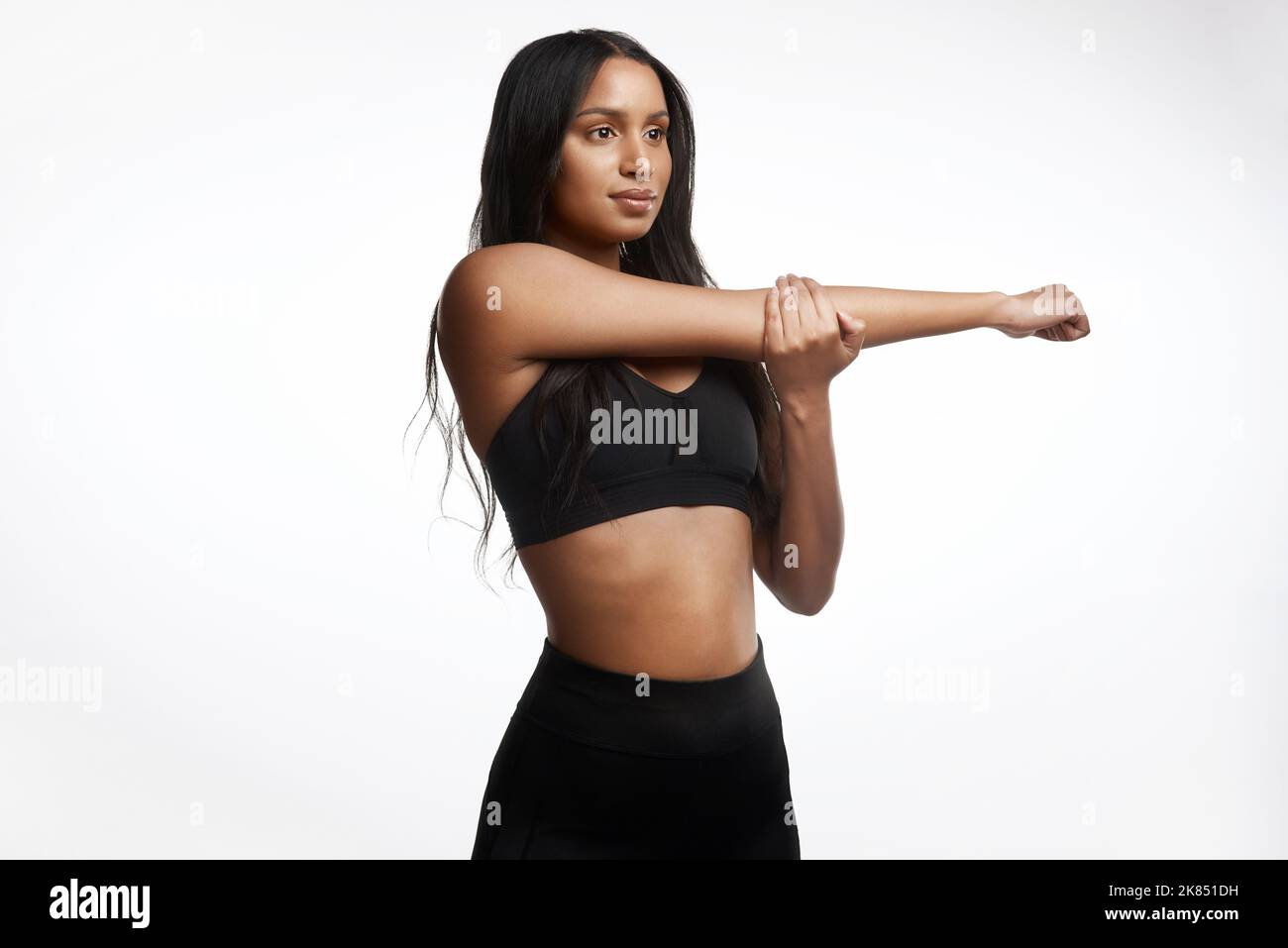 Richtig dehnen kann Muskelkater verringern. Studioaufnahme einer sportlichen jungen Frau, die ihre Arme vor weißem Hintergrund streckt. Stockfoto