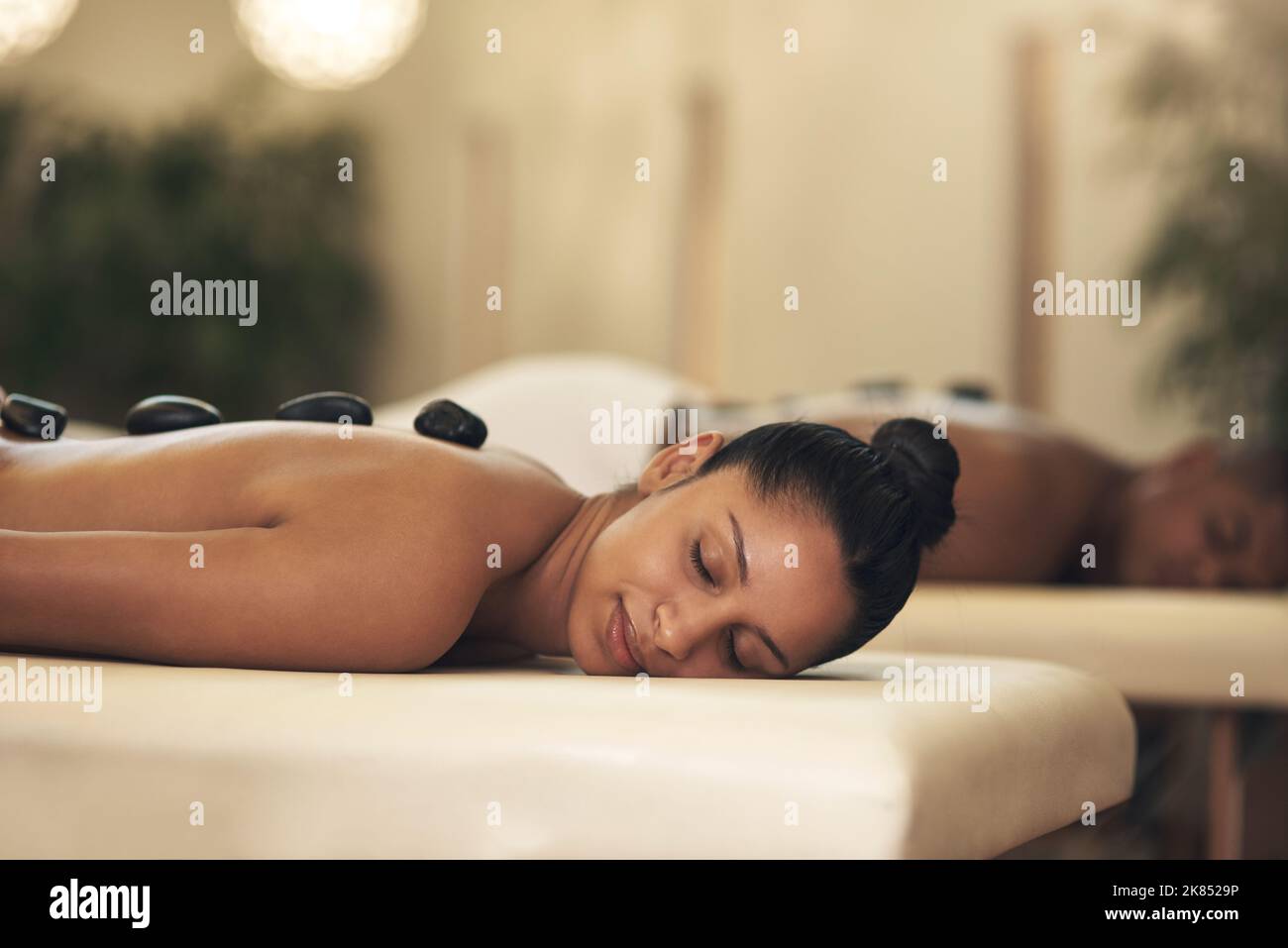 Buchen Sie sich einen Wellnesstag - Sie werden begeistert sein. Eine junge Frau bekommt eine Hot Stone Massage in einem Spa. Stockfoto