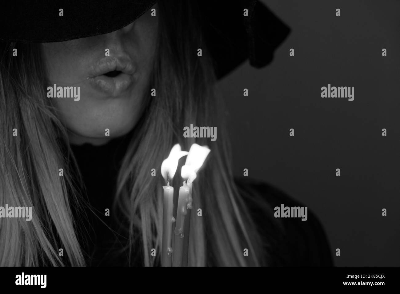 Ein Mädchen in einem schwarzen Hut im Dunkeln hält eine Kerze, ein Mädchen mit Kerzen in der Nacht Stockfoto