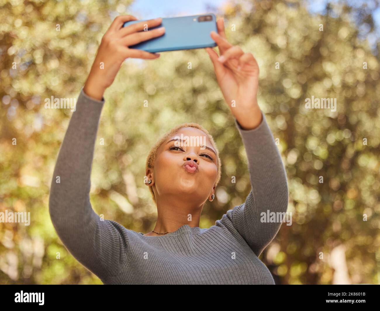 Schwarze Frau, Telefon und Selfie mit Put im Park mit Sonnenschein, Sommer und Glück von Bäumen. Frau, Smartphone und Lippen im Kuss für Foto, im Freien Stockfoto