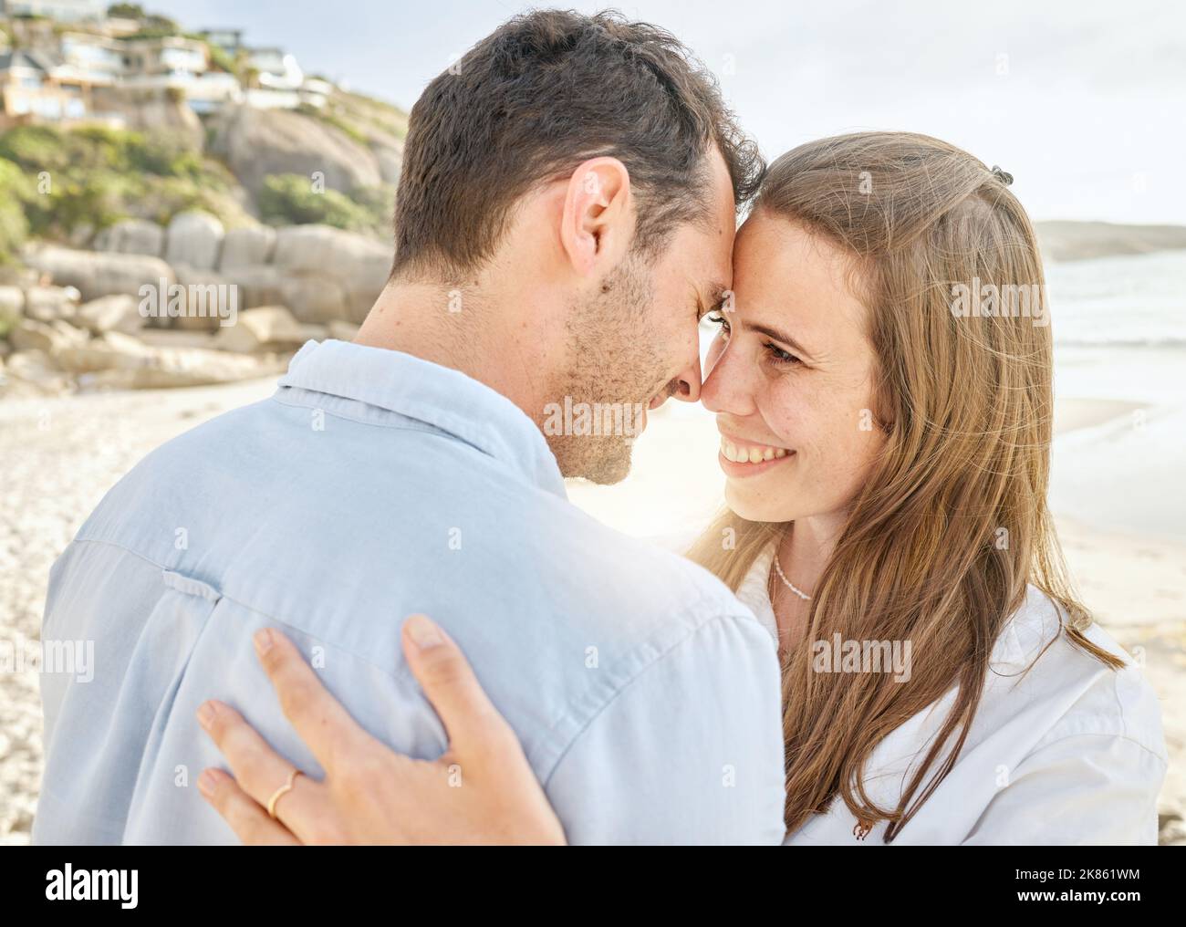 Paare, lieben und umarmen Sie sich gemeinsam am Strand für eine Verlobungsreise oder einen Hochzeitstag am Meer. Junger Mann und Frau lächeln glücklich und romantisch Stockfoto