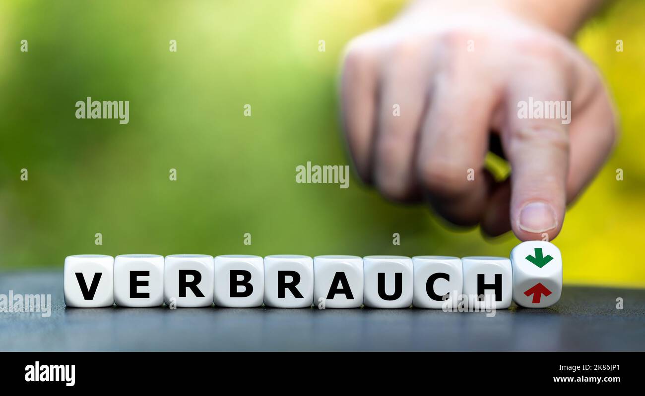 Symbol zur Reduzierung des Verbrauchs während der Energiekrise. Hand dreht Würfel und ändert die Ausrichtung eines Pfeils von oben nach unten neben dem Deutschen Stockfoto