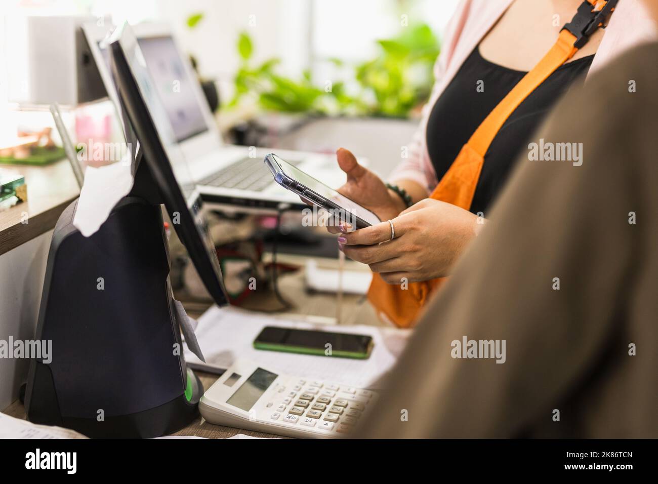 Frau, die am Kassiererschalter im Café, Kleinunternehmereinzelhandel, mit dem Mobiltelefon telefoniert. Stockfoto