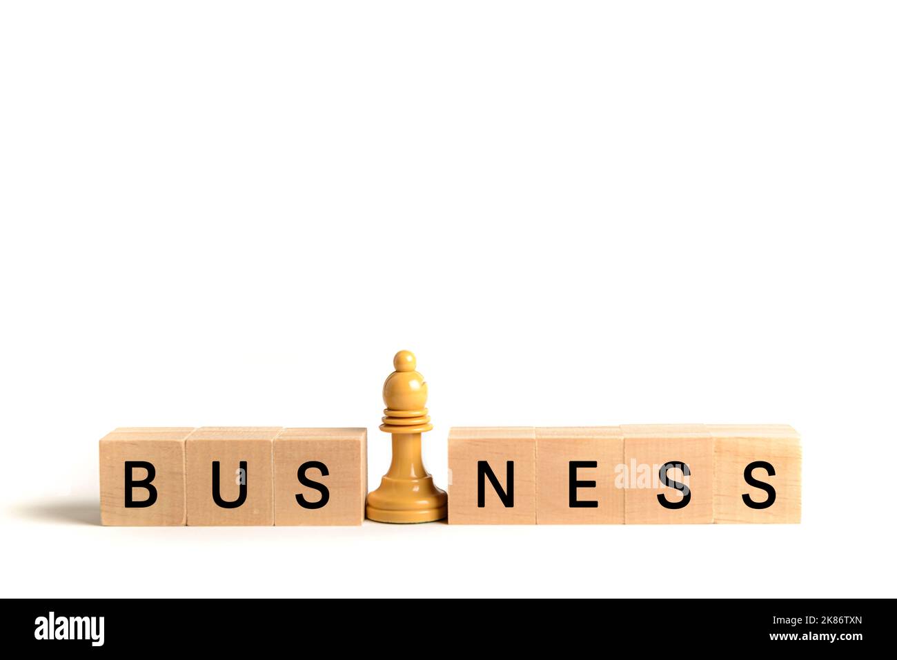 Weißer Schachbischof neben Holzblöcken, die das Wort 'Business' bilden, auf weißem Hintergrund. Bild zur Veranschaulichung des Konzepts von Führung und Geschäft Stockfoto