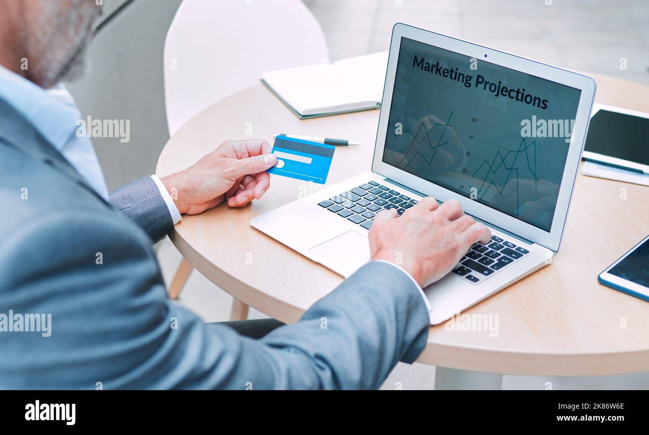 Setzen Sie das Geld für etwas Marketing. Nahaufnahme eines nicht erkennbaren Geschäftsmannes, der einen Laptop und eine Kreditkarte bei der Arbeit auf dem Balkon des verwendet Stockfoto