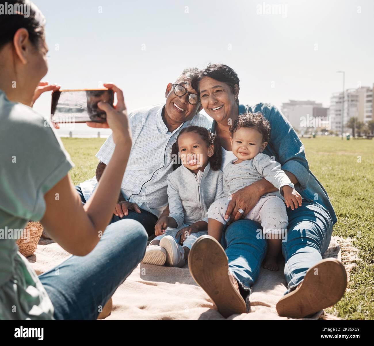 Großeltern, Kinder und Mutter mit Foto am Telefon im Sommer gemeinsam im Park. Entspannen Sie sich, glücklich und lächeln Sie von Kindern und älteren Männern und Frauen mit Stockfoto