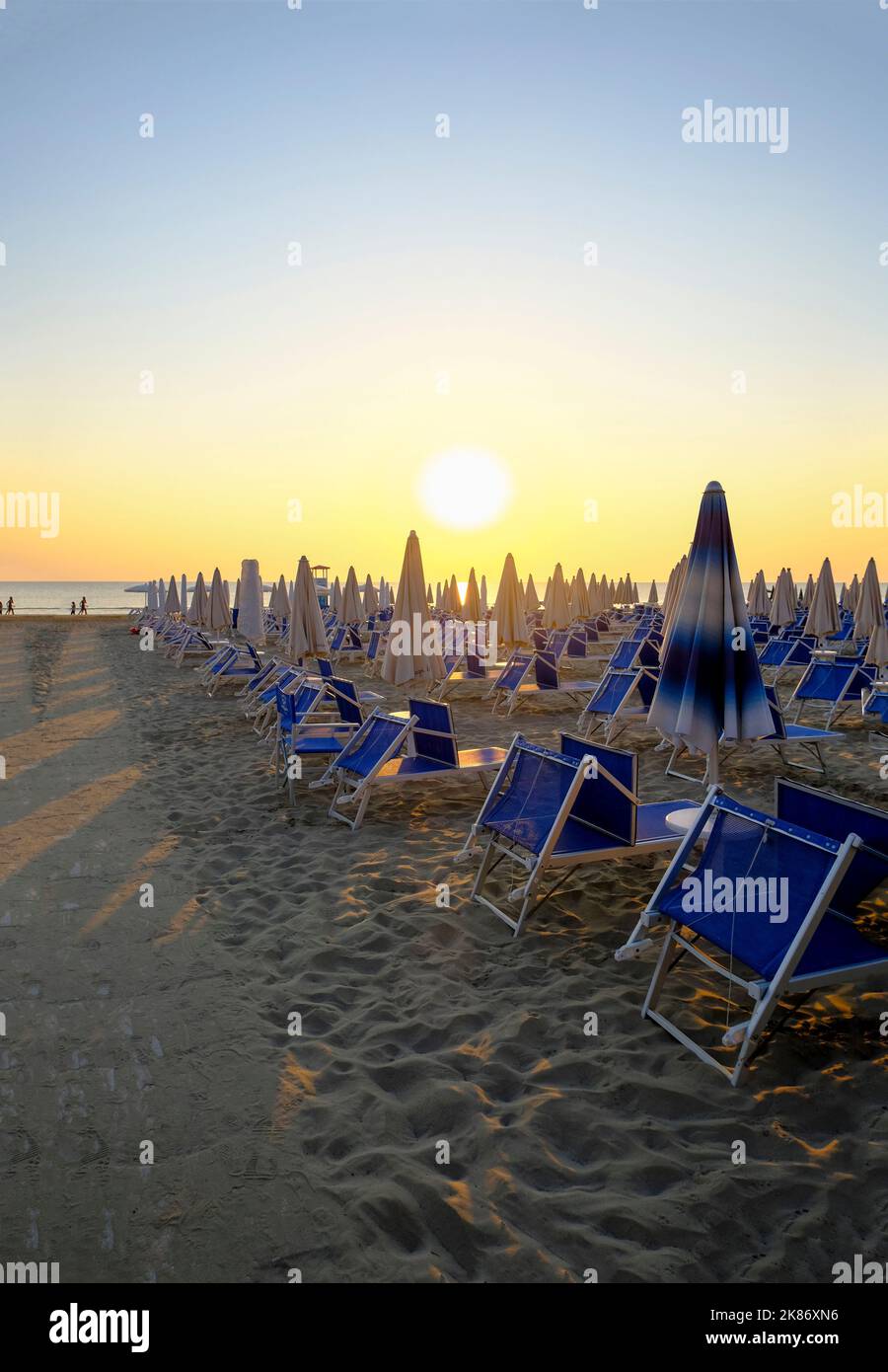 Sonnenschirme und Sonnenliegen am Strand über dem Sonnenaufgangshimmel. Weg auf dem Sand zum Strand. Sommerurlaub Hintergrund. Senigallia, Italien Stockfoto