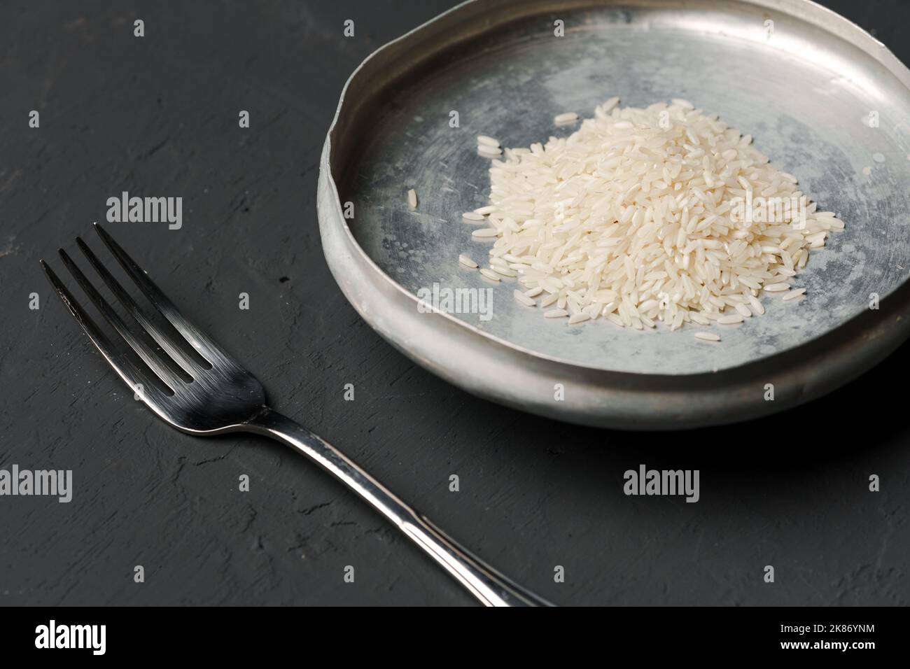 Haufen von trockenem Reis in einer Schüssel auf schwarzem Hintergrund, Mangel an Nahrung, Hunger-Konzept Stockfoto