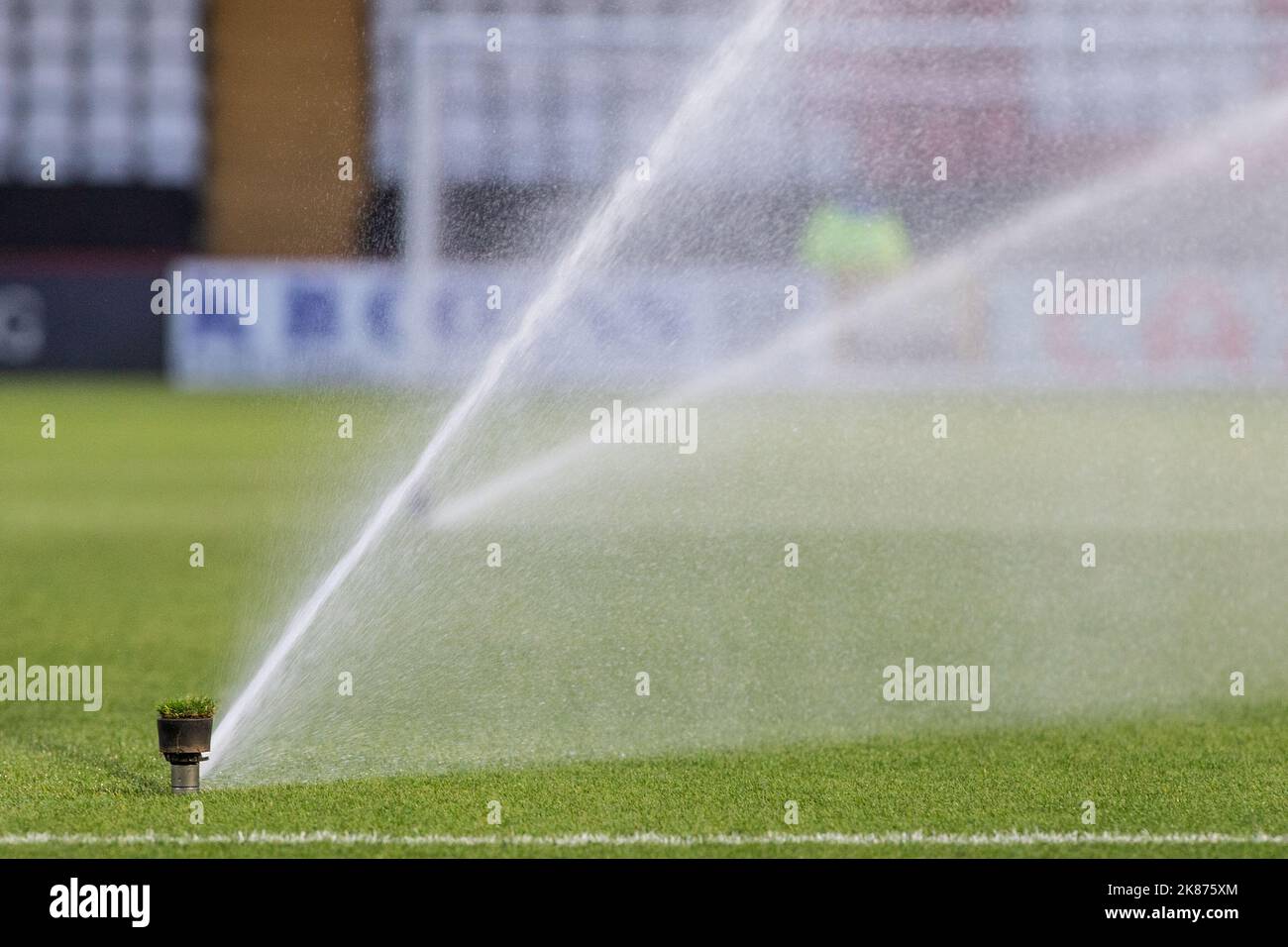 Pop-up-Sprinkler, die Wasser auf den Platz im englischen Fußballstadion der unteren Liga sprühen. Stockfoto
