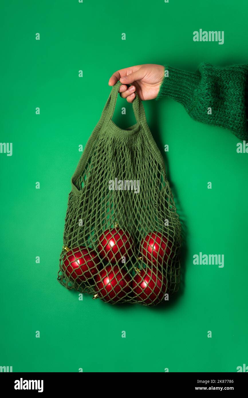 Trendy minimale Idee des neuen Jahres Poster, String-Tasche mit roten weihnachtskugeln in der Hand auf grünem Hintergrund. Minimales weihnachtskonzept Stockfoto