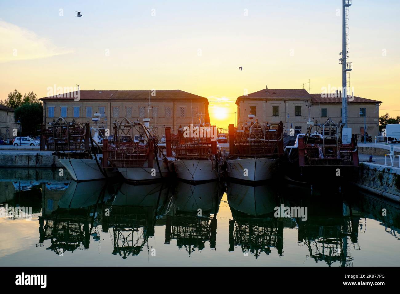 Küste und Skyline der Stadt bei Sonnenuntergang in Senigallia, Marken, Italien. Stadthintergrund. Wasserspiegelungen, Wellen in den Abendlichtern Stockfoto