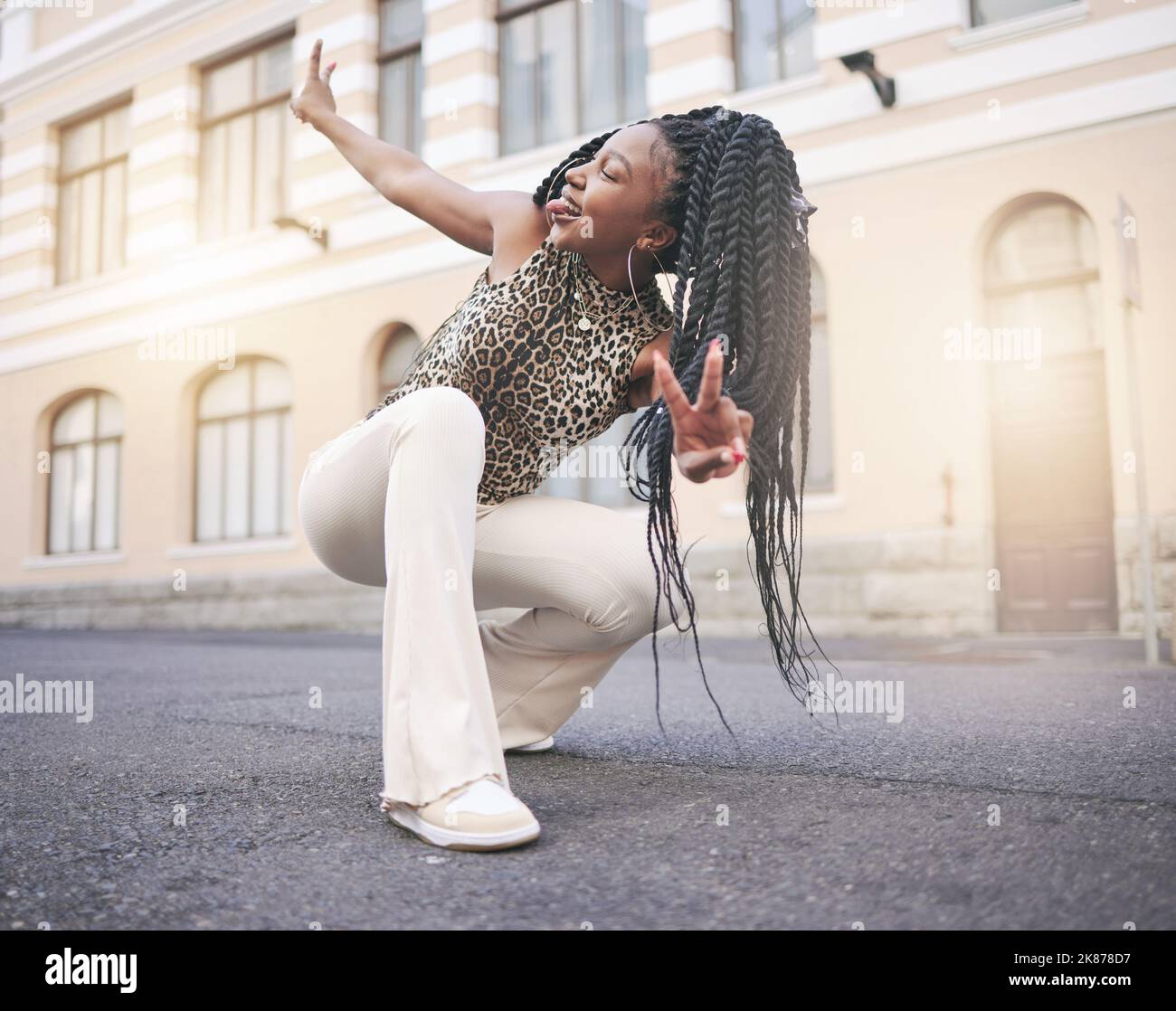 Schwarze Frau, Street Fashion und Frieden Hand Zeichen in der Stadt, hocken und Zunge aus in einzigartigen Selbstausdruck. Gen z, trendy und cool, kreativ und urban Stockfoto