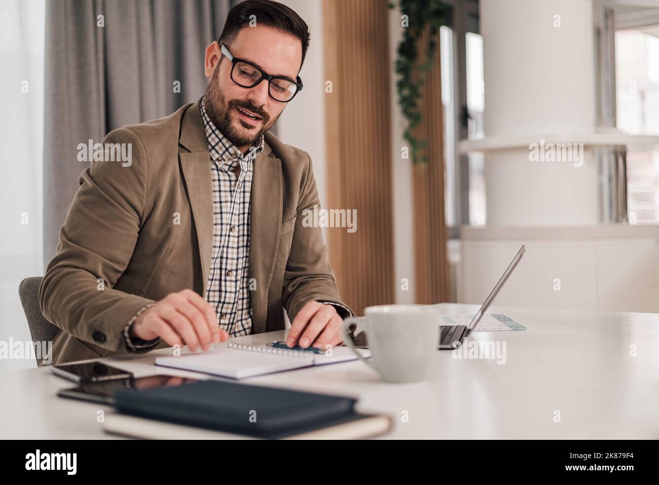 Ehrgeiziger, erwachsener Büroangestellter, der das Büro verlässt und dafür sorgt, dass sein Schreibtisch ordentlich und sauber ist. Stockfoto