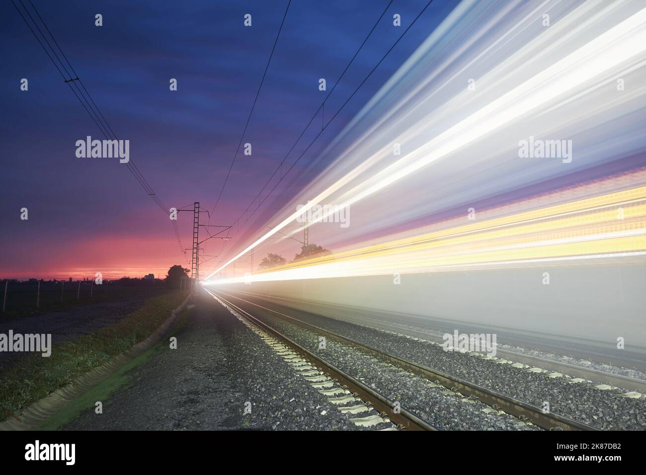 Moderne Eisenbahn bei schönem Sonnenaufgang. Leichte Spur des Hochgeschwindigkeitszuges auf der Eisenbahnstrecke. Umzug moderner Intercity-Personenzug. Stockfoto