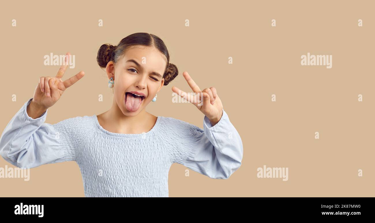 Lustige stilvolle preteen Mädchen mit Spaß ragen aus ihrer Zunge und zeigt beide Hände V-Zeichen. Stockfoto
