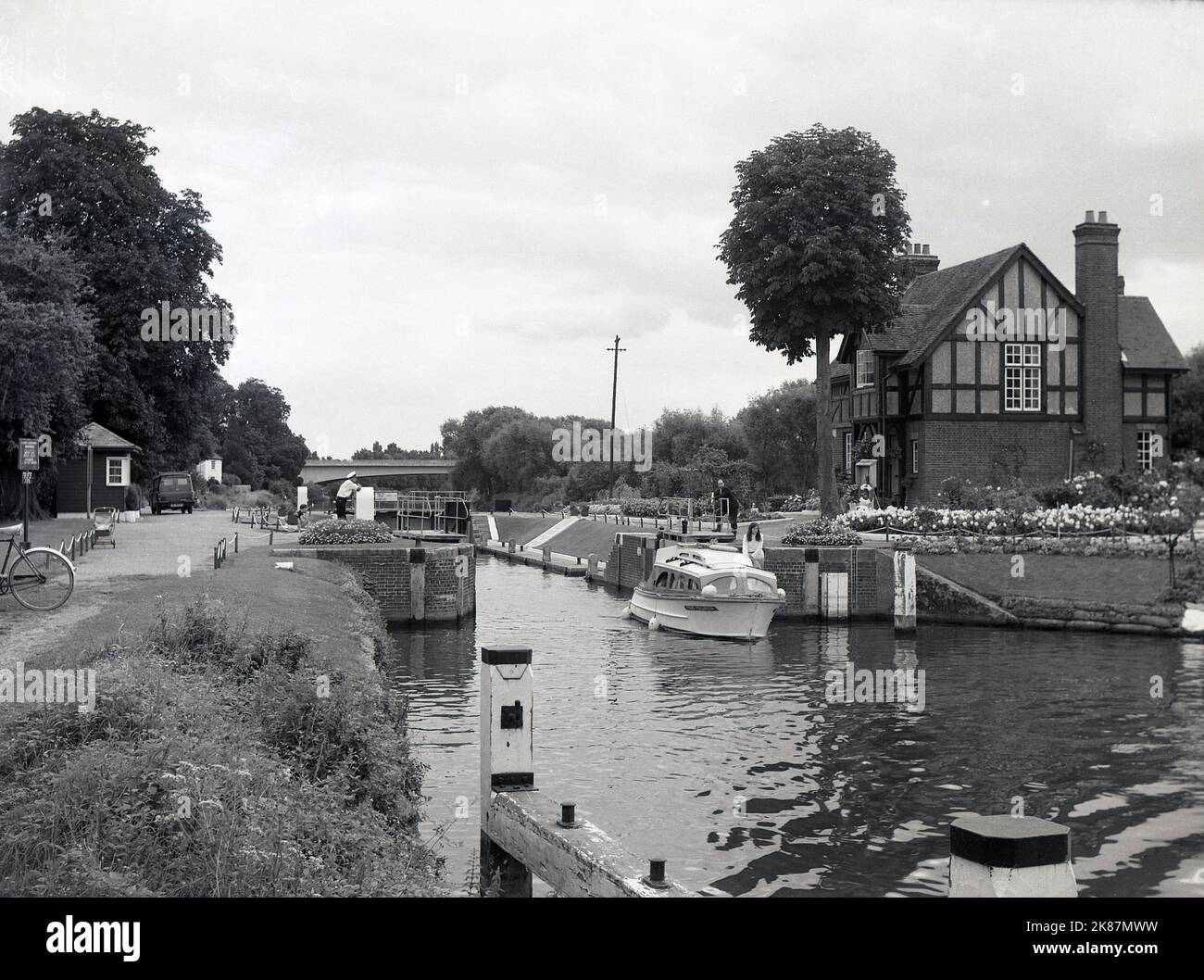 1966, historisch, ein Boot, das durch die Bray-Schleuse auf der Themse am Windsor & Eton-Flussufer, England, Großbritannien, fährt, mit der Schleusenwärterhütte auf der Insel zwischen der Schleuse und dem Wehr, rechts auf dem Bild zu sehen. Das grassseitige Schloss wurde 1845 gebaut. Stockfoto