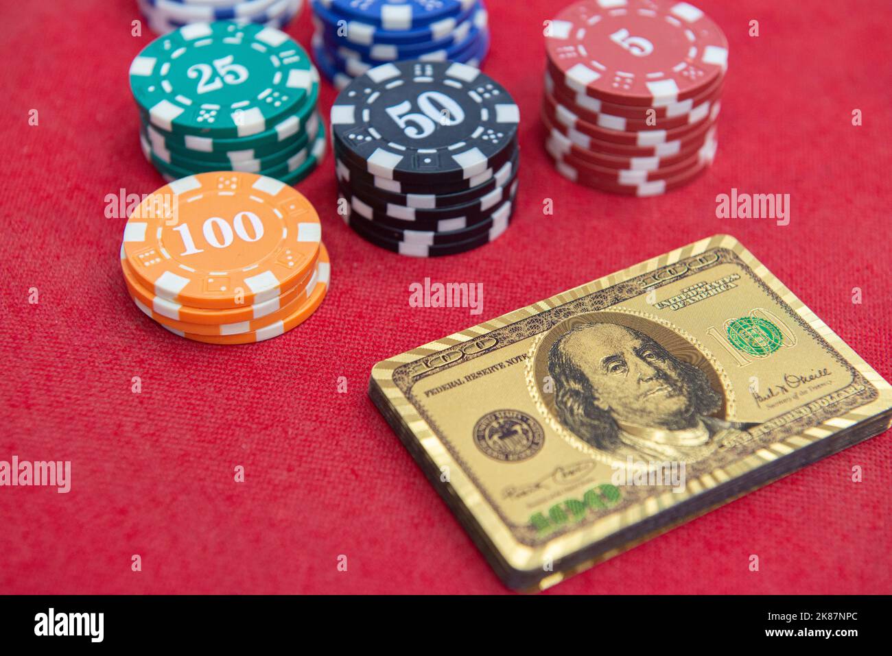 Draufsicht auf goldene 100-Dollar-Spielkarten neben Chips-Stapeln auf dem roten Filztisch. Poker-Spiel ist eines der beliebtesten Kartenspiele der Welt ein Stockfoto
