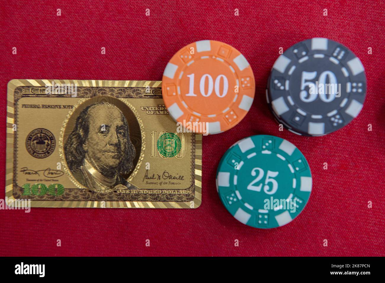 Draufsicht auf goldene 100-Dollar-Spielkarten neben Chips-Stapeln auf dem roten Filztisch. Poker-Spiel ist eines der beliebtesten Kartenspiele der Welt ein Stockfoto