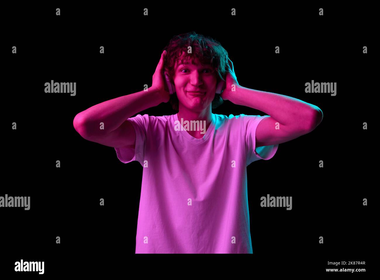 Halblanges Porträt eines jungen Mannes mit schockiertem Gesichtsausdruck, der isoliert auf dunklem Hintergrund in violettem Neonlicht gestikelt wird. Emotionen, Jugend, Verkauf Stockfoto