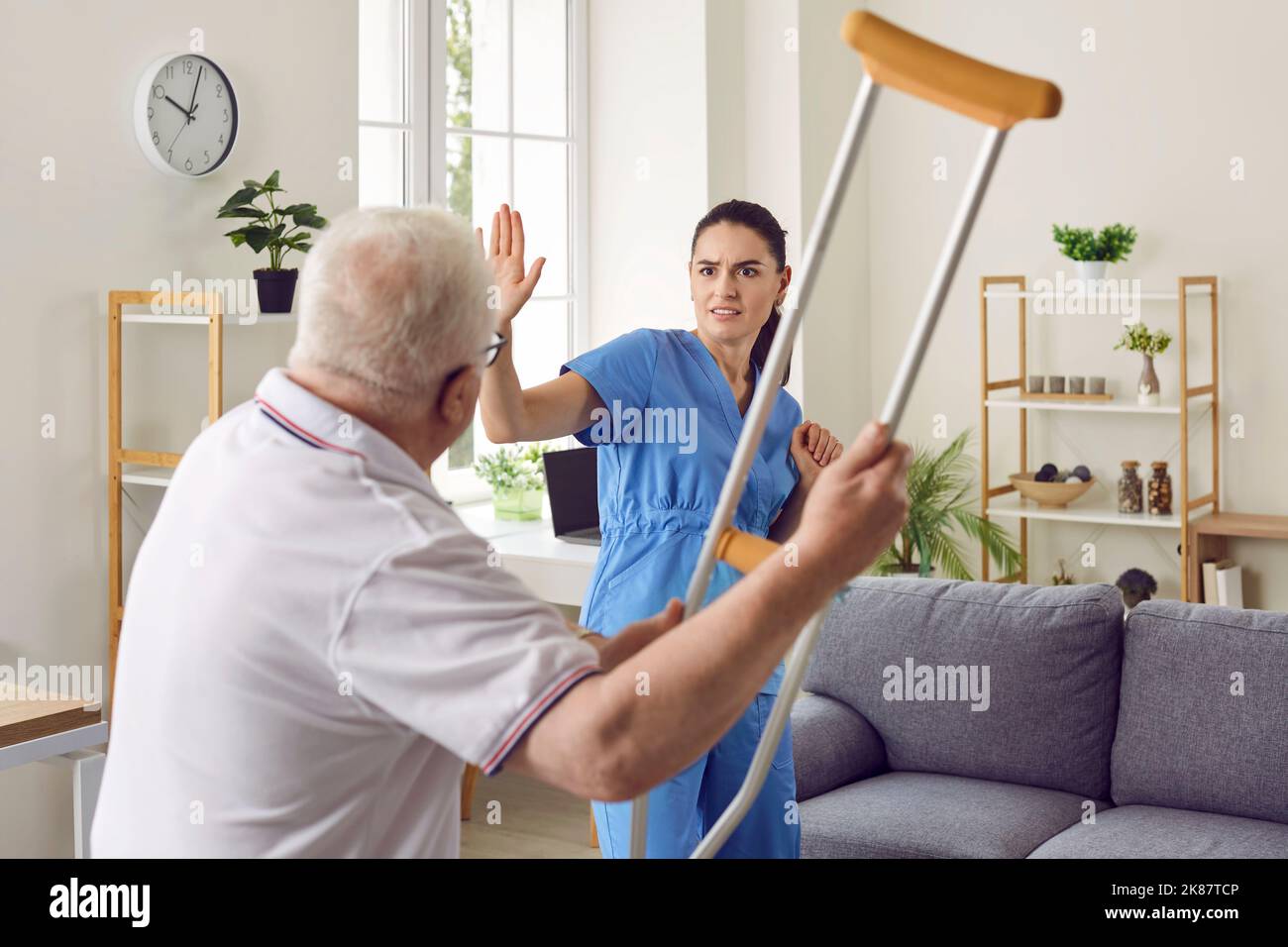 Wütender, aggressiver Seniorpatient will kämpfen und bedroht die Krankenschwester mit seiner Krücke Stockfoto