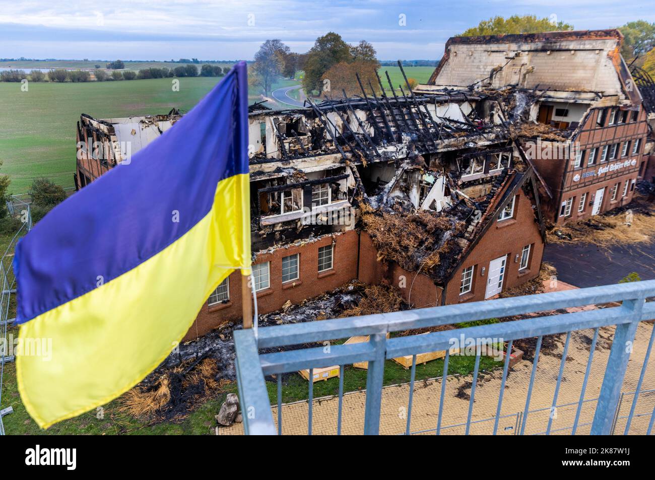 Deutschland. 21. Oktober 2022. 21. Oktober 2022, Mecklenburg-Vorpommern, Groß Strömkendorf: Die ukrainische Flagge fliegt auf dem Dach eines Nebengebäudes vor den Überresten des verbrannten Hotelgebäudes. Das Gebäude, in dem Flüchtlinge aus der Ukraine untergebracht wurden, brannte in der Nacht von 19 auf 20.10.2022 vollständig ab. Niemand wurde beim Feuer verletzt, Brandstiftung wird vermutet. Die 14 Bewohner wurden nach den Rettungsarbeiten in anderen Wohnungen untergebracht. Foto: Jens Büttner/dpa Quelle: dpa picture Alliance/Alamy Live News Stockfoto