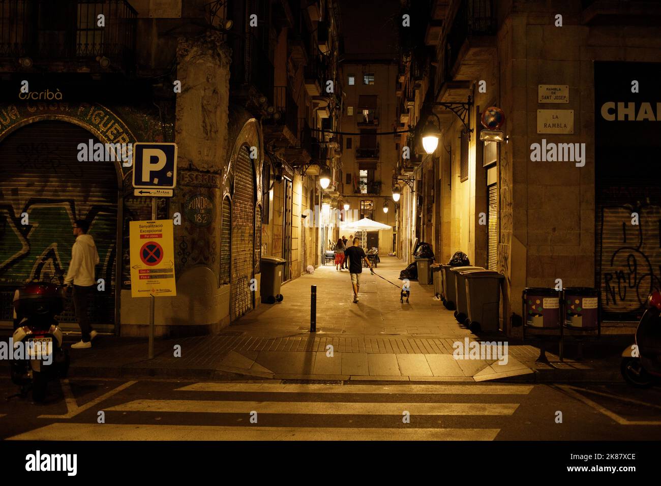 Ein Mann, der nachts in einer Seitenstraße vor der Rambla in Barcelona, Spanien, mit seinem Hund läuft Stockfoto