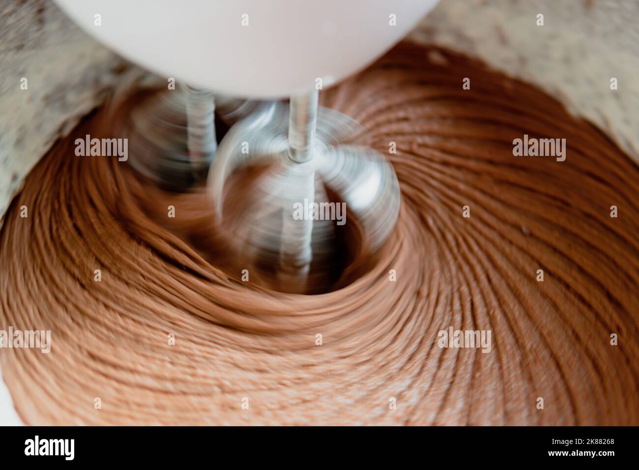 Nahaufnahme des Schokoladenkuchen-Teigs in einer Rührschüssel mit sich drehenden Quirlen. Stockfoto