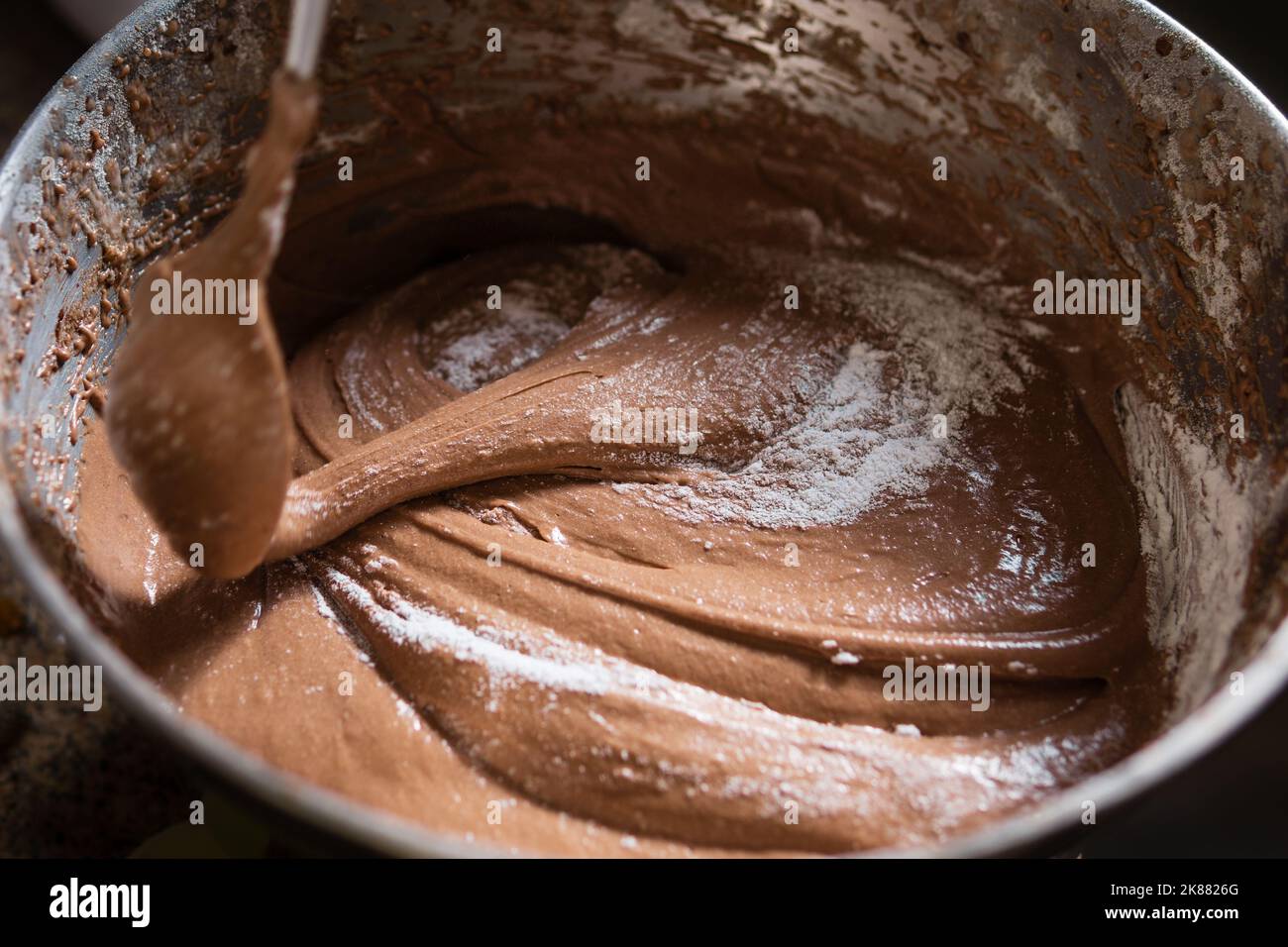 Nahaufnahme eines Löffels, der Schokoladenkuchenteig und Zucker in einer Rührschüssel rührt. Stockfoto