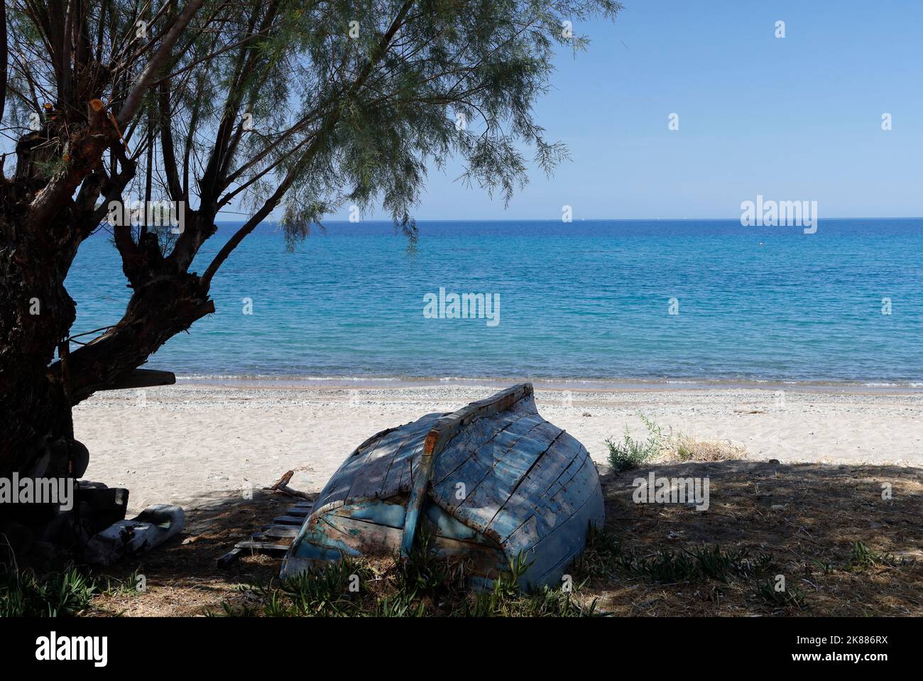 Altes umgedrehtes griechisches Ruderboot am Strand im Schatten eines Tamarisken. Lesbos. Oktober 2022. Herbst. Stockfoto