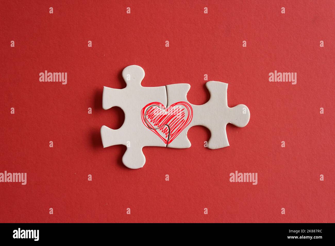 Draufsicht Bild der verbundenen Puzzle-Stücke mit rotem Herz-Symbol auf rotem Hintergrund. Liebe und Beziehung Konzept Stockfoto