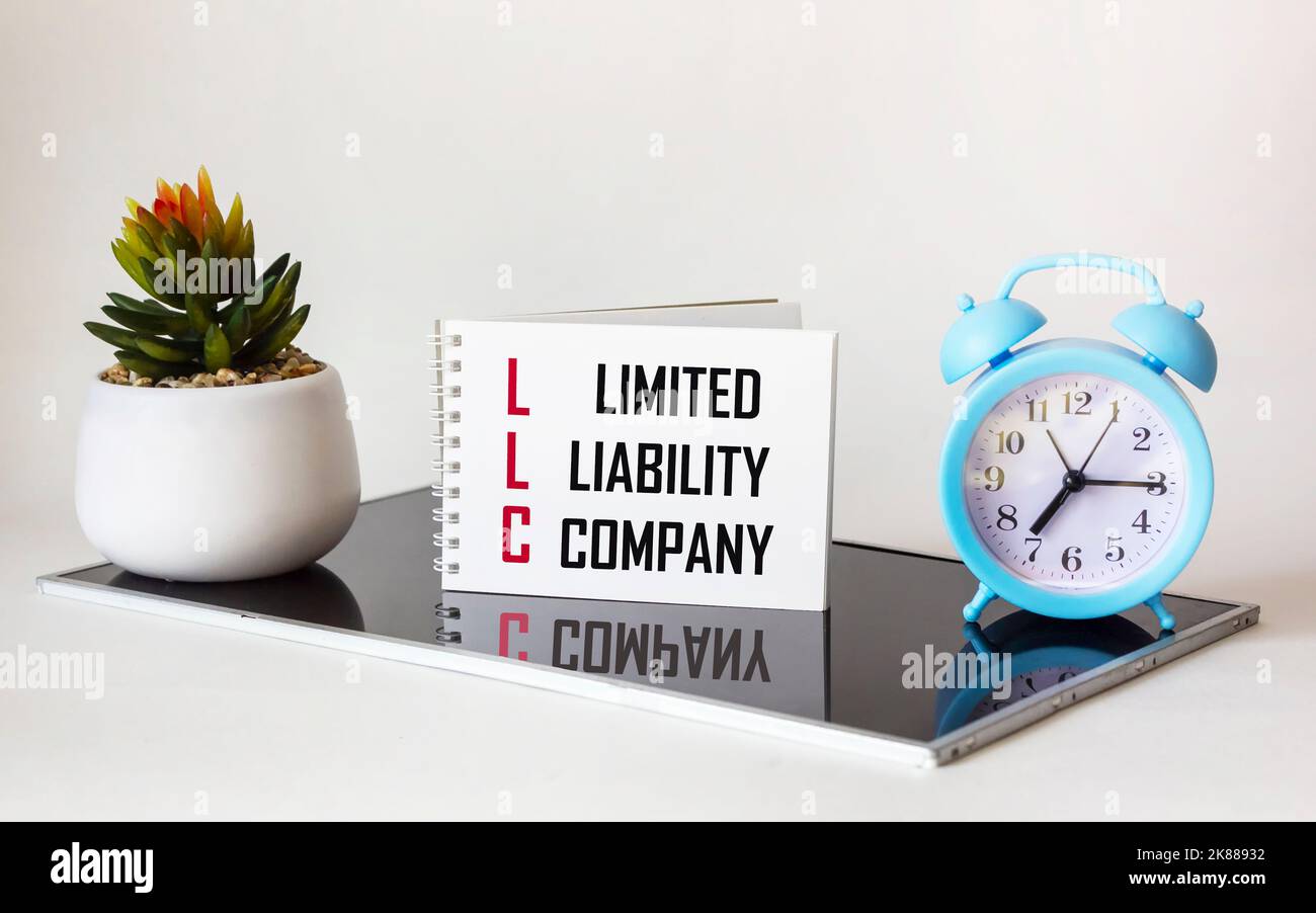Geschäfts- und Finanzkonzept. Auf einem weißen und schwarzen Tisch gibt es eine Uhr, einen Kaktus und ein Notizbuch, auf dem es steht - GESELLSCHAFT MIT BESCHRÄNKTER HAFTUNG Stockfoto