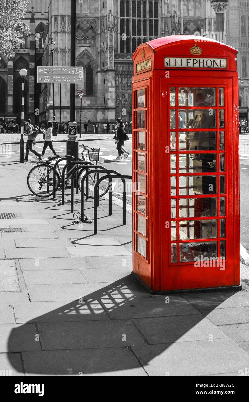 Eine selektive Farbe einer roten Telefonzelle mit grauer Stadt und Menschen im Hintergrund. Stockfoto