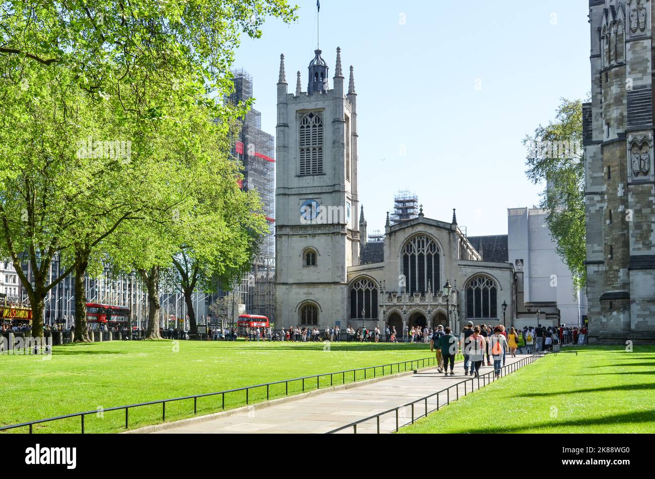 Blick auf das Westminster Abbey Gebäude in London, Großbritannien, mit Menschen, die auf einem grünen Park spazieren gehen und rote Busse parken. Stockfoto