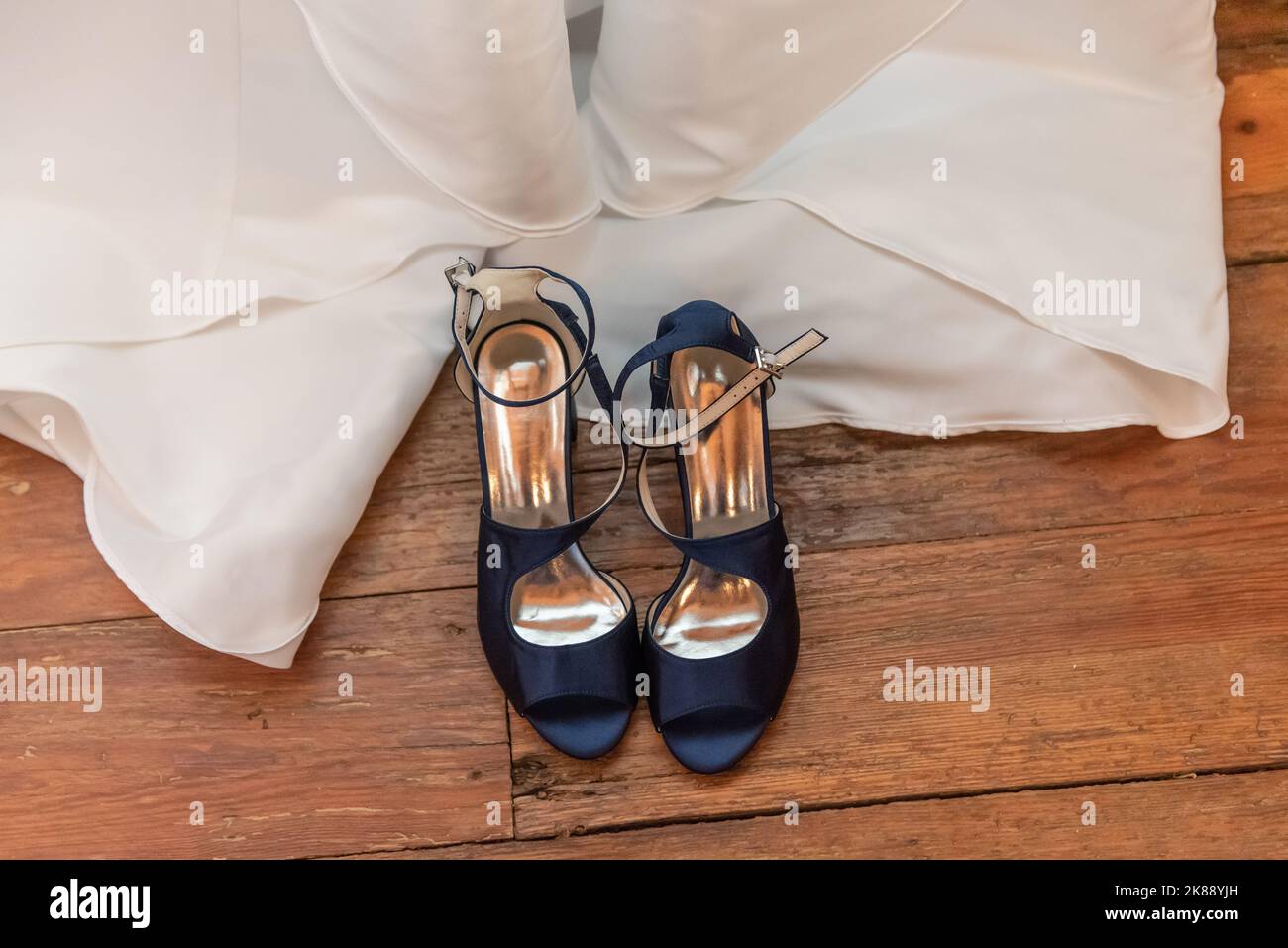 Blick von oben auf die offenen Schuhe der Braut sind entschnallt und neben dem Hochzeitskleid angelegt. Stockfoto