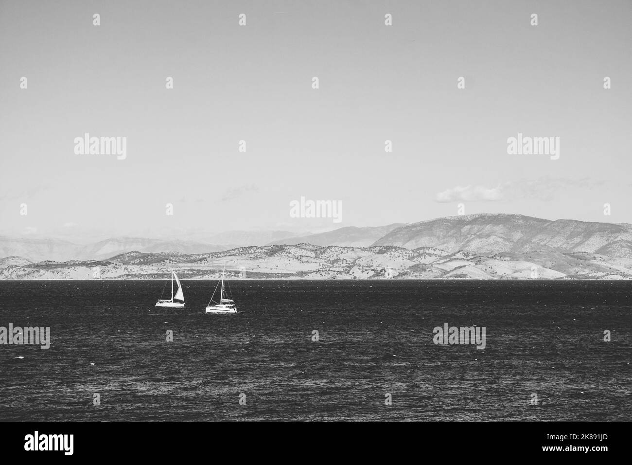 Schöne Aussicht auf die griechischen Berge am blauen Wasser, auf dem zwei weiße Segelboote segeln. Stockfoto