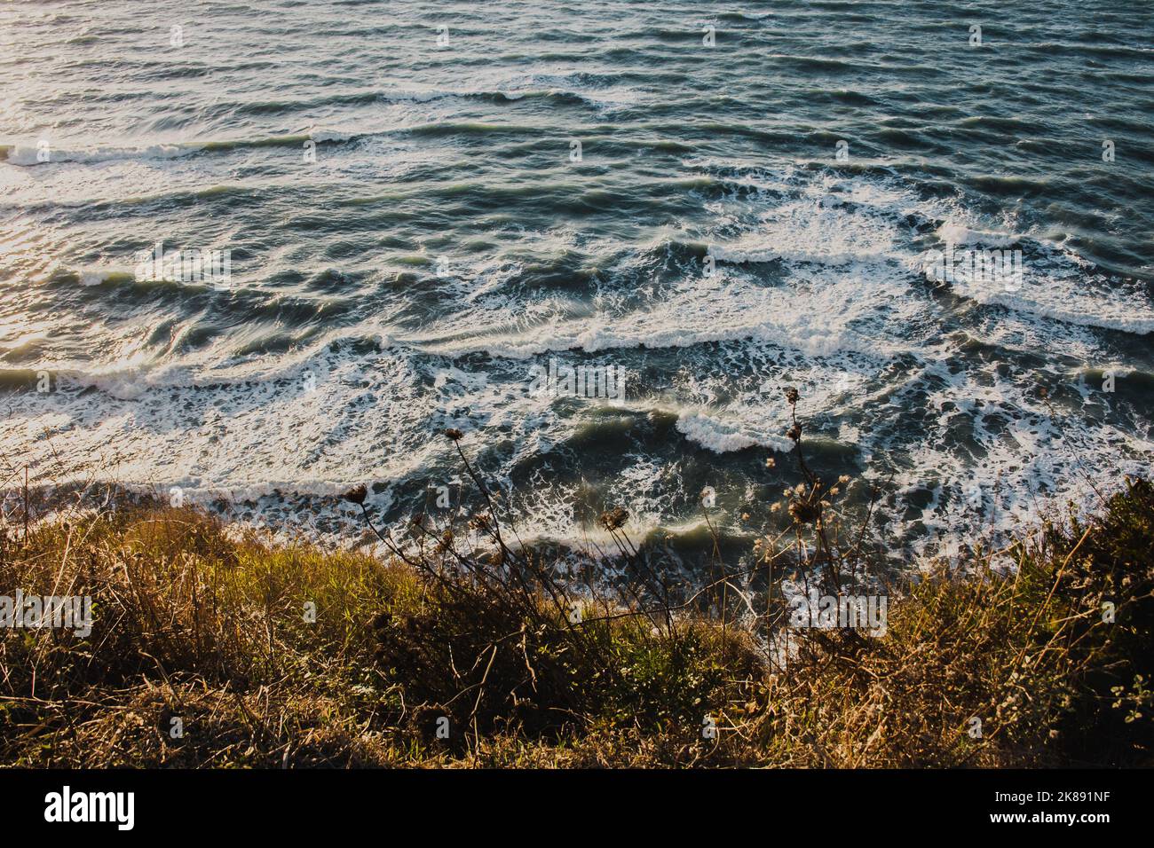 Blick auf blaues Wasser mit riesigen Wellen und weißem Schaum, der an der Küste in der Sandsteinfelsenwand zusammenbricht. Stockfoto