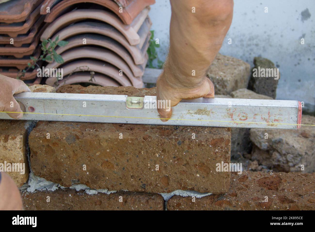 Bild von den Händen eines Bauarbeiters, der mit einer Ebene die Präzision der Verlegung von Tuffsteinen für den Bau einer Wand überprüft. Stockfoto