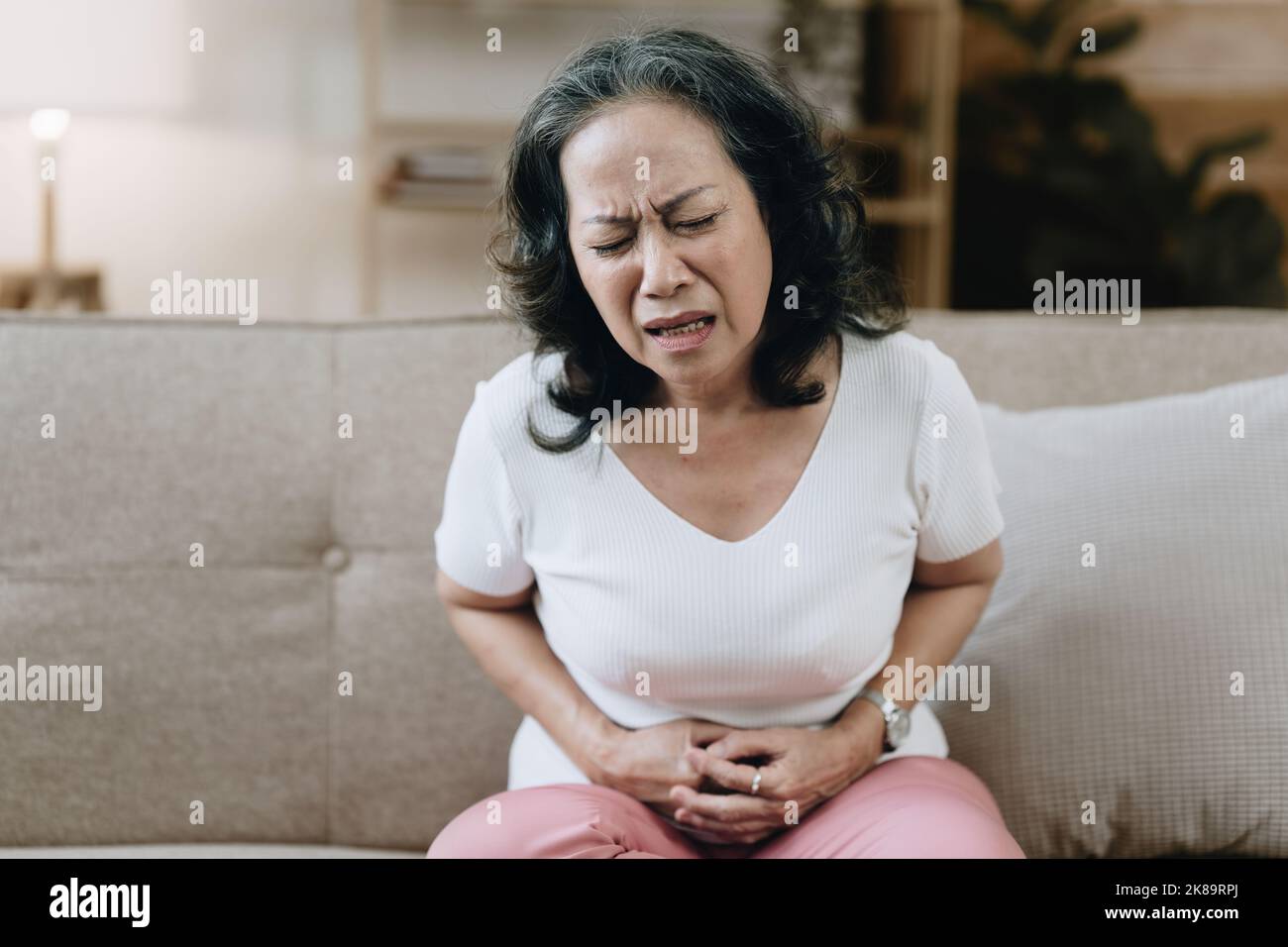 Die Asiatin in den Achtzigern, erschöpft und unter Stress, ist mit Magenschmerzen zu Hause Stockfoto