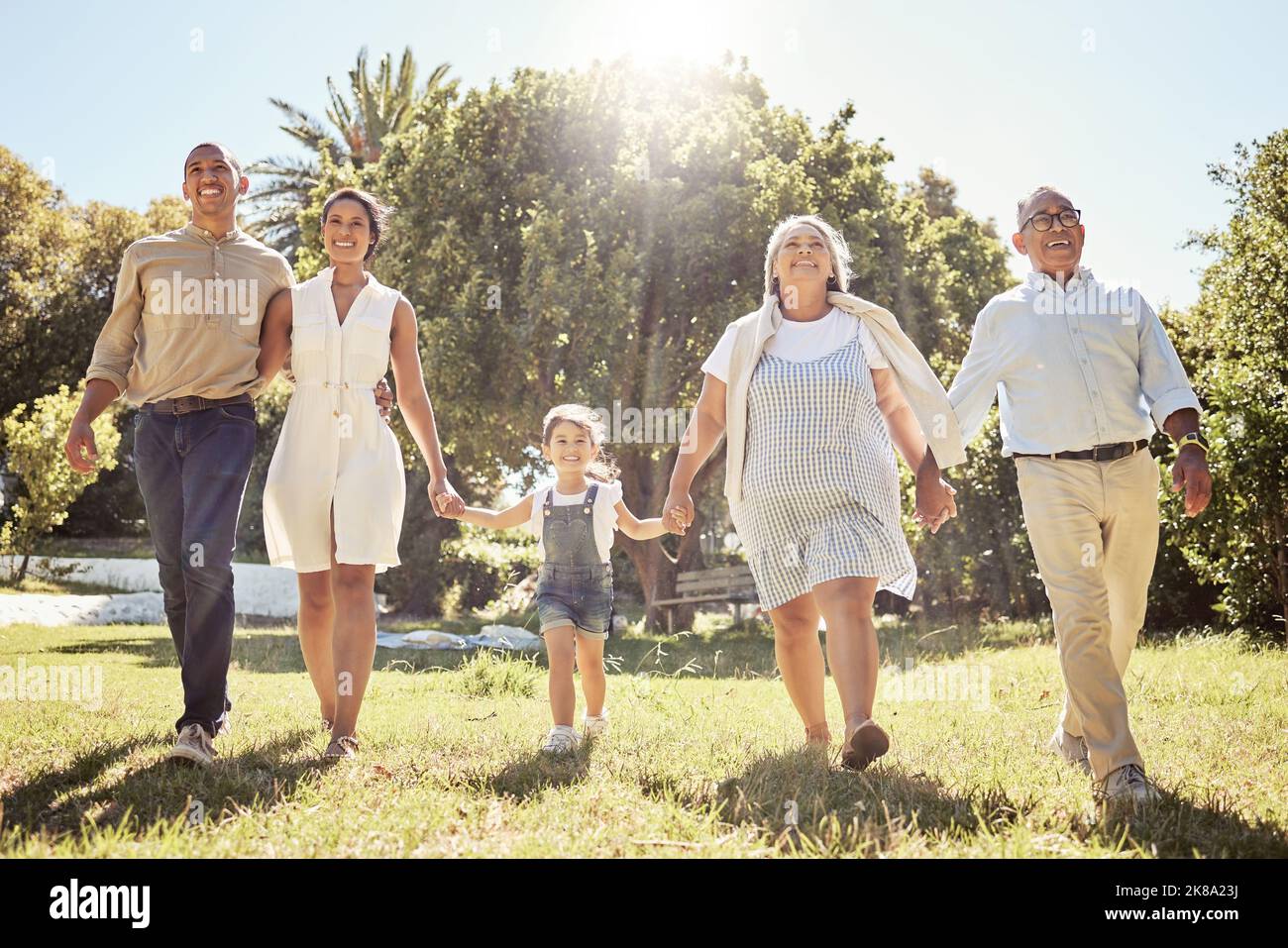 Schwarze glückliche Familie, die Hände hält und im Naturpark zusammen im Sommerurlaub im Freien spazieren geht. Großeltern, Eltern und Kinder haben Spaß in der Sonne Stockfoto
