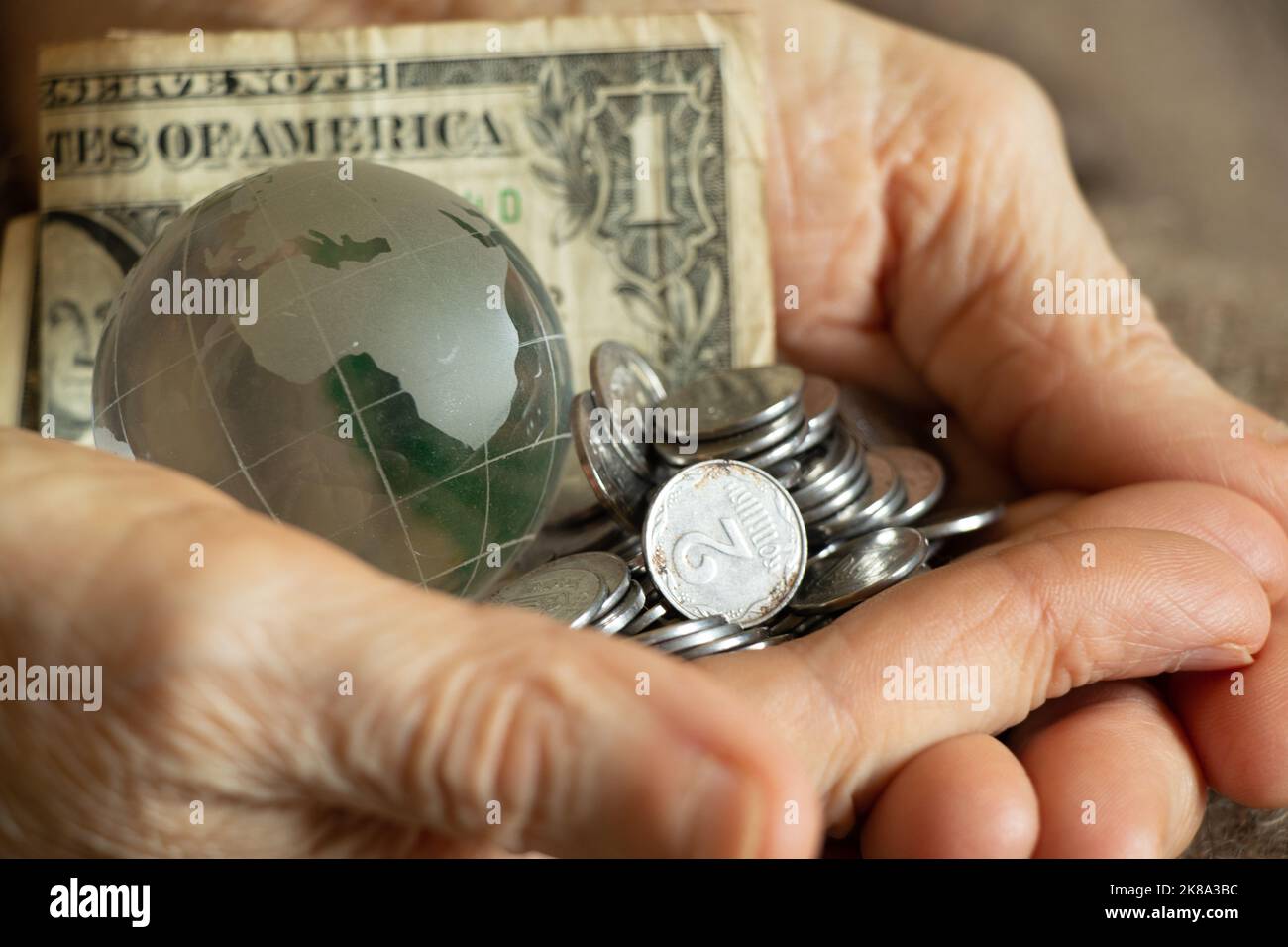 Amerikanische Dollars und ukrainische Pennies und eine Glaskugel des Planeten liegen in den Händen einer alten Frau, Finanzwelt und Menschen Stockfoto