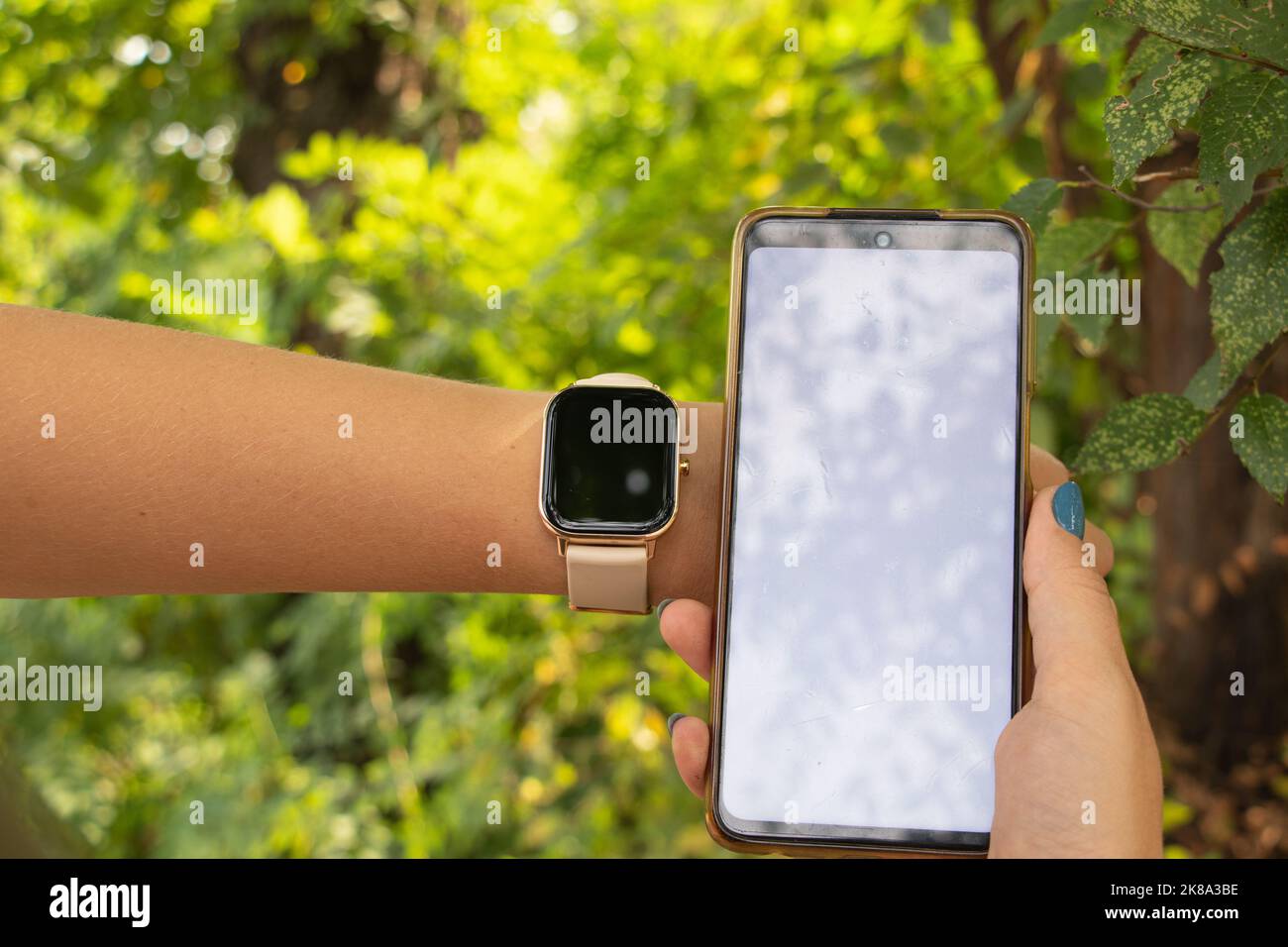 Smart Watch und ein Telefon mit einem weißen Bildschirm in den Händen eines Mädchens im Park, neue Technologien und Menschen, eine Uhr und ein Telefon Stockfoto