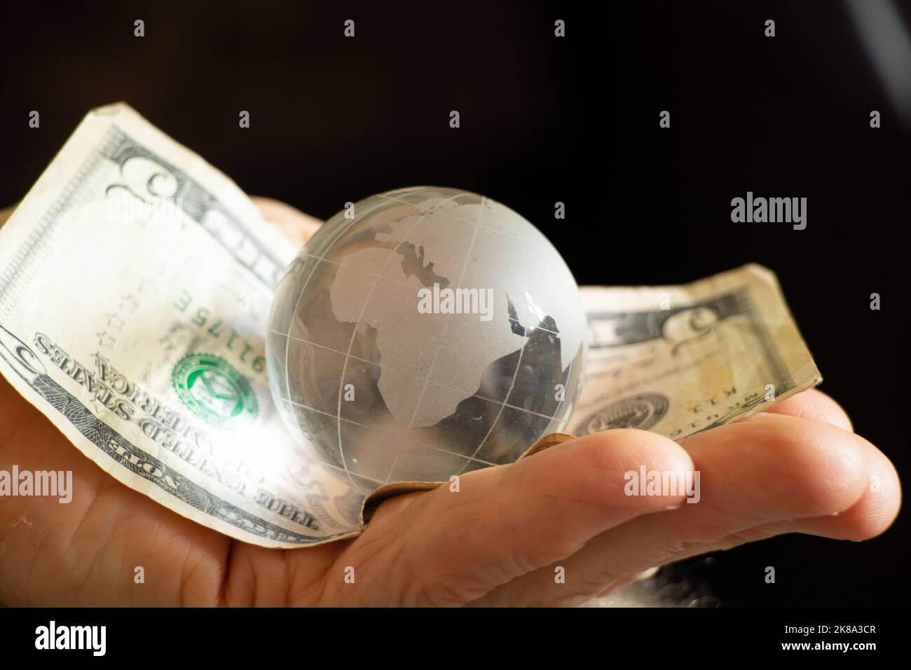 amerikanische Dollar und eine Glaskugel des Planeten liegen in den Händen einer alten Frau, Finanzwelt und Menschen Stockfoto